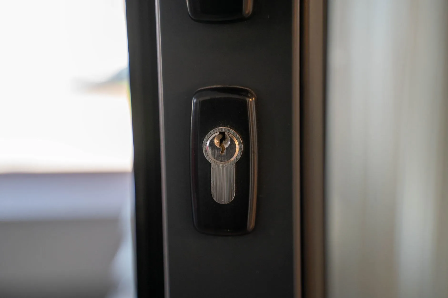 A euro cylinder lock set into a dark aluminium door frame, close up