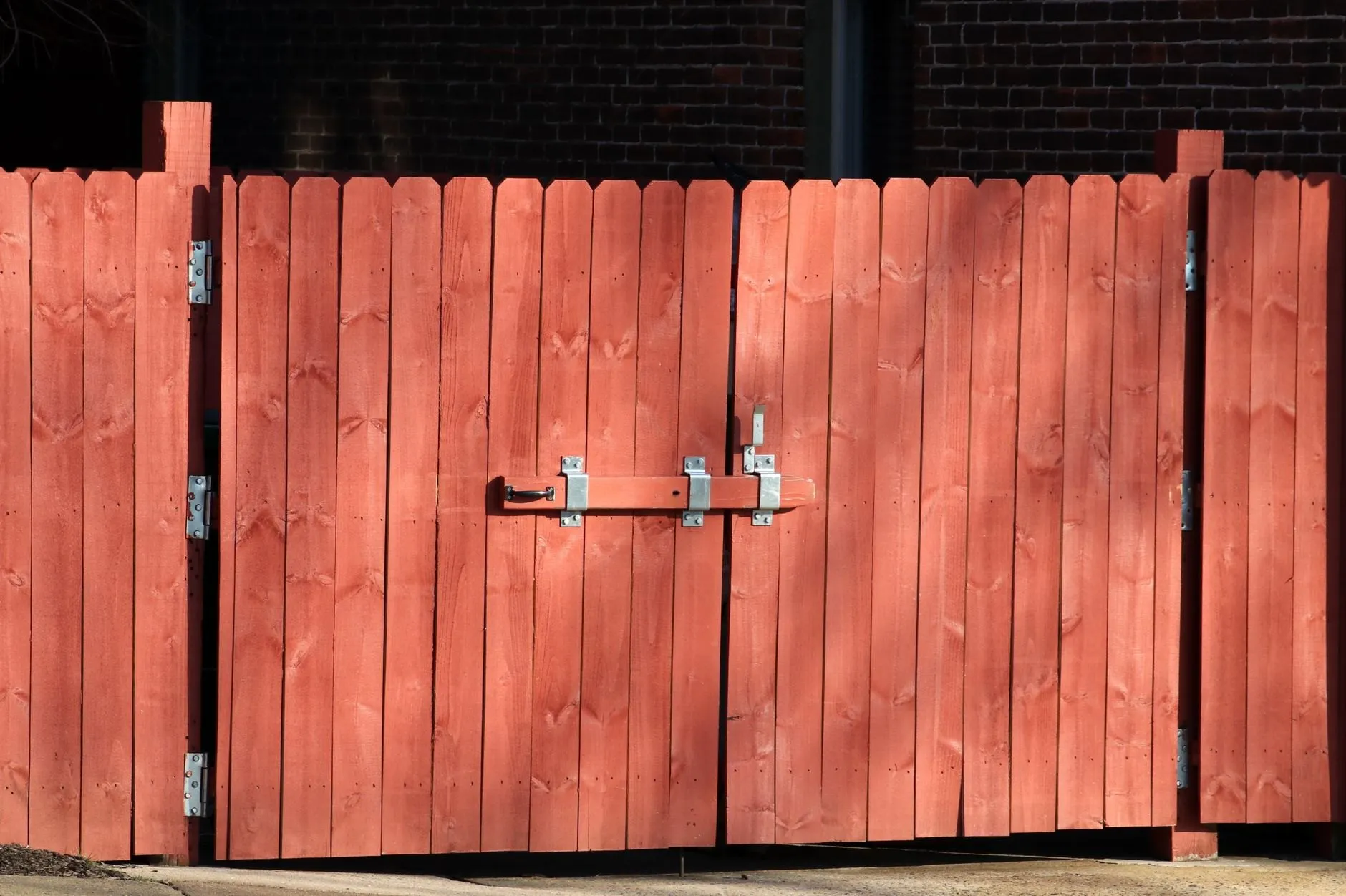 A galvanised drop bar and latch across a red-painted timber garden gate