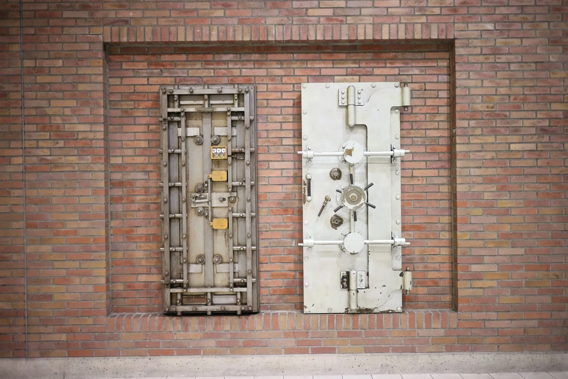 Two old steel vault doors set into a brick wall, showing their bolt work